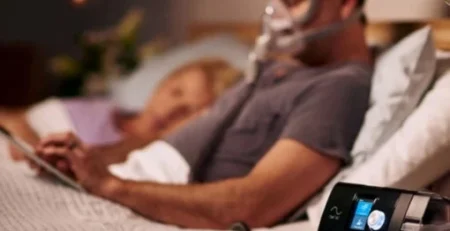 Barbat citind in pat cu Aparat Auto CPAP, AirSense 10 AutoSet cu umidificator, ResMed