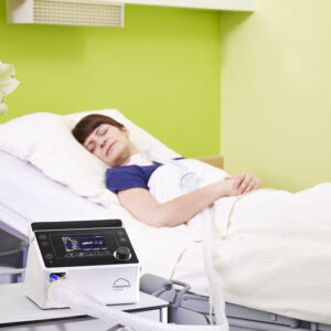 Femeie dormind in pat cu Ventilator prisma VENT40 terapie invaziva cu canula traheala